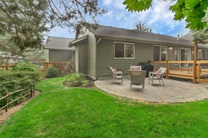 A residential property with a covered patio, two wicker chairs, a wooden deck, and a well-maintained lawn.