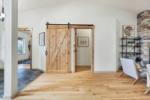 Una habitación con piso de madera, puerta corredera estilo granero, chimenea de piedra y una silla.