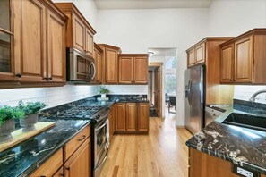A modern kitchen with wooden cabinets, stainless steel appliances, and a black marble countertop.