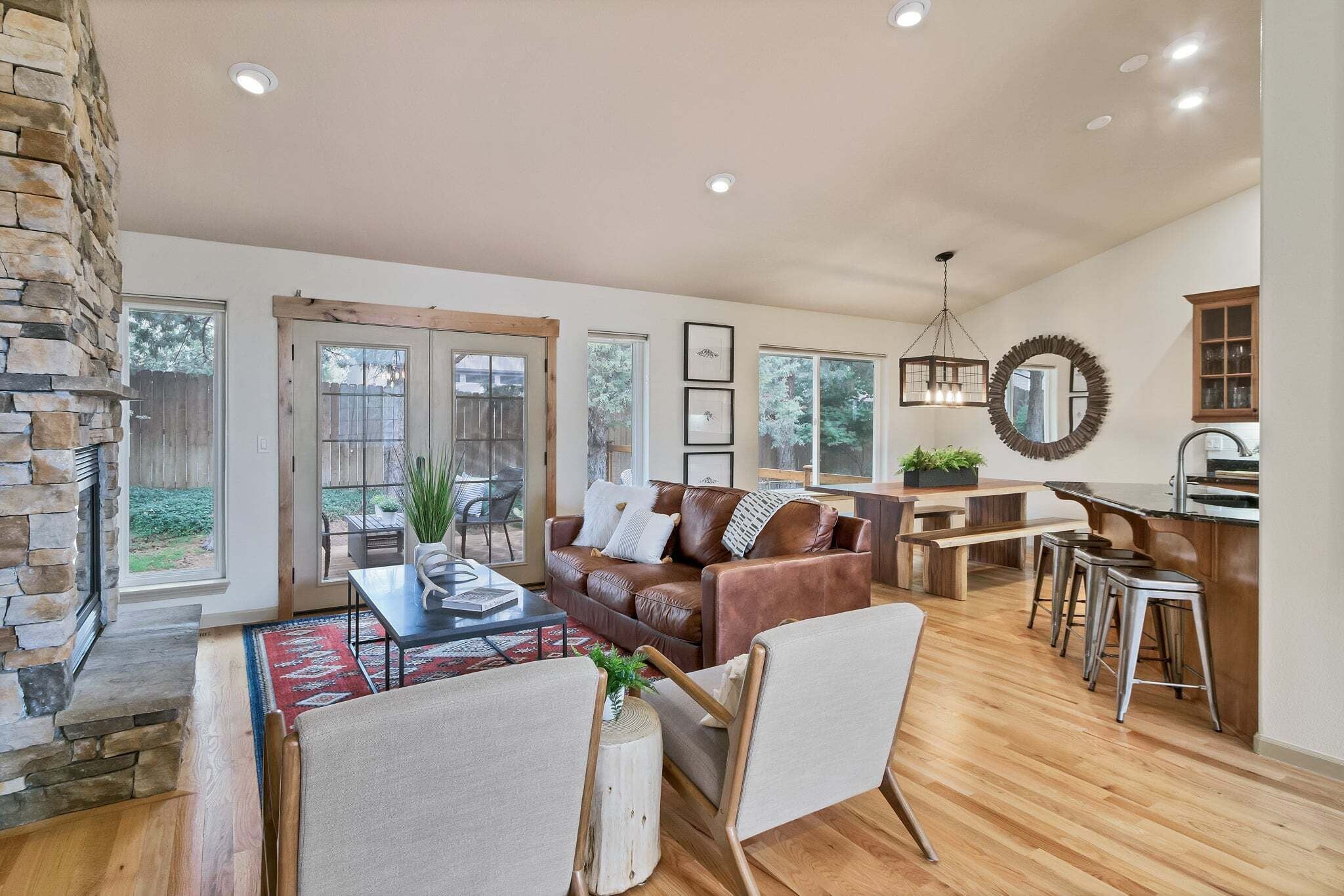 A spacious living room with a stone fireplace, a brown leather sofa, and a dining area with a wooden table and bar stools.