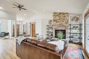 A spacious living room with a stone fireplace, leather sofa, and a ceiling fan.