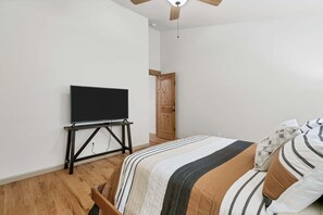 Ein Schlafzimmer mit einem Bett, einem Flachbildfernseher auf einem Standfuß, einer Holztür und einem Deckenventilator.