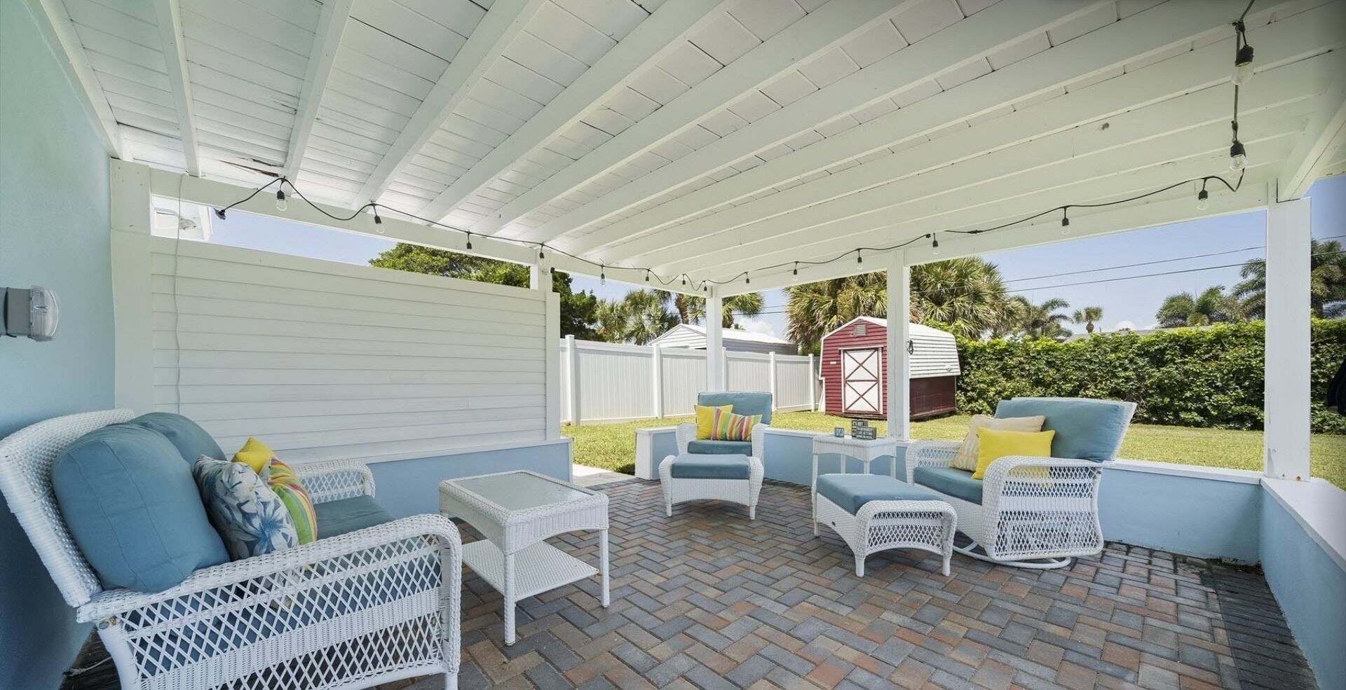 A covered patio area with wicker furniture, a small table, and a red shed in the background.