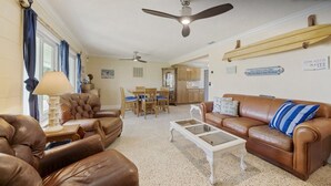 A spacious living room with leather sofas, a coffee table, and a ceiling fan. - Beautiful, Private Beach House - 1 Block To The Beach - AC  3 Bedroom - Sleeps 8 (Cocoa Beach)