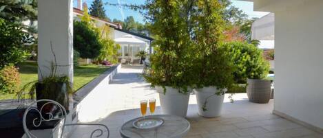 Un patio con dos mesas redondas y sillas, plantas en macetas y una casa al fondo.