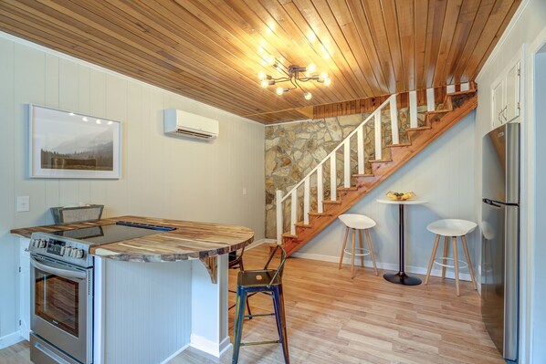 A kitchen with a wooden ceiling, a stone wall, and a wooden staircase.