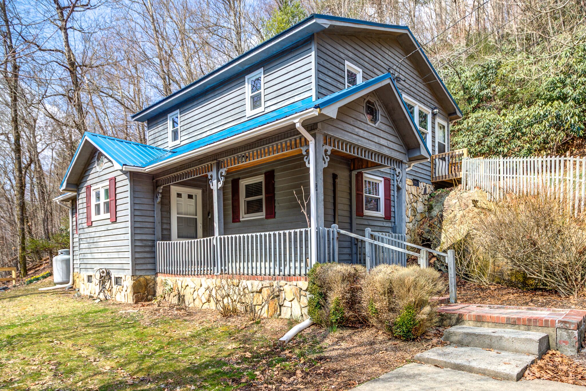 A two-story house with a stone foundation, a blue roof, and a porch with a white railing.