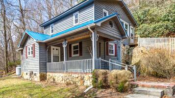 A two-story house with a stone foundation, a blue roof, and a porch with a white railing.