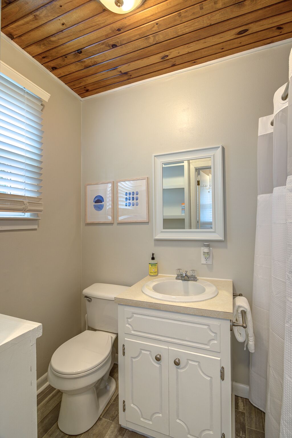 A bathroom with a wooden ceiling, a toilet, a sink with a mirror, and a shower curtain.