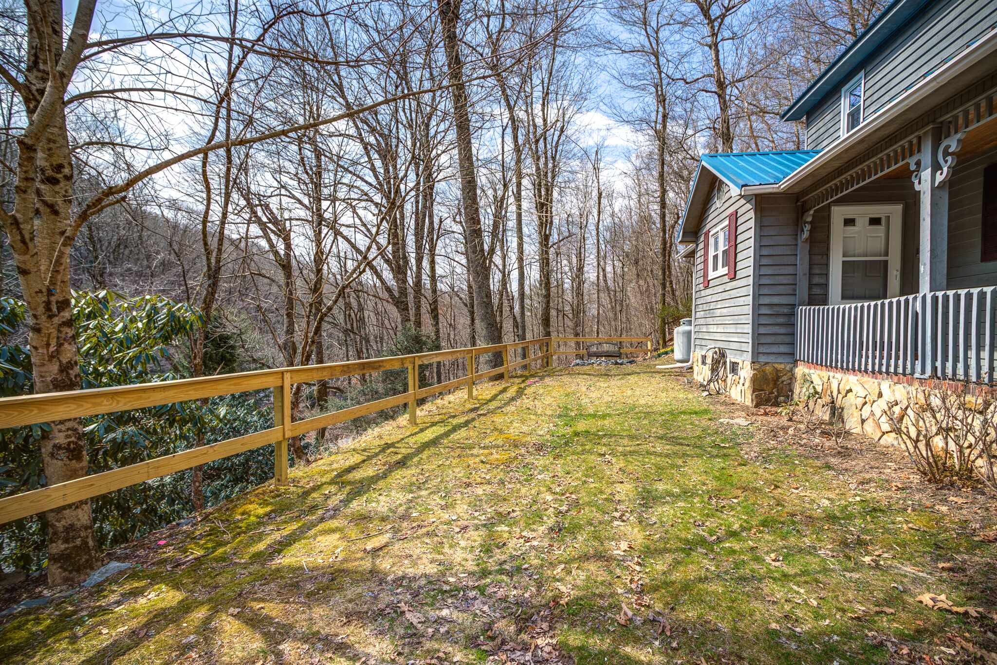A wooden deck leading to a house with a stone foundation and a blue roof.