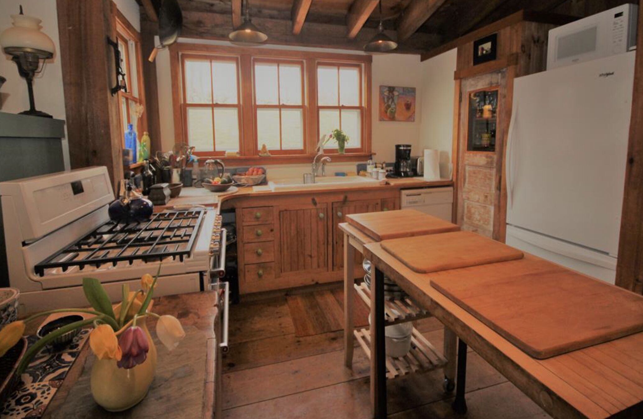 A rustic kitchen with wooden cabinets, a gas stove, a sink, and a refrigerator.