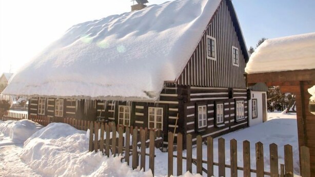 Une maison en bois avec un toit enneigé et une clôture en bois à l’avant.