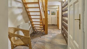 Un couloir avec un escalier en bois, une chaise en osier, un radiateur et une porte derrière laquelle se trouve un autre radiateur.