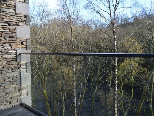 Een balkon met een stenen muur en glazen hekwerk met uitzicht op een bebost gebied.