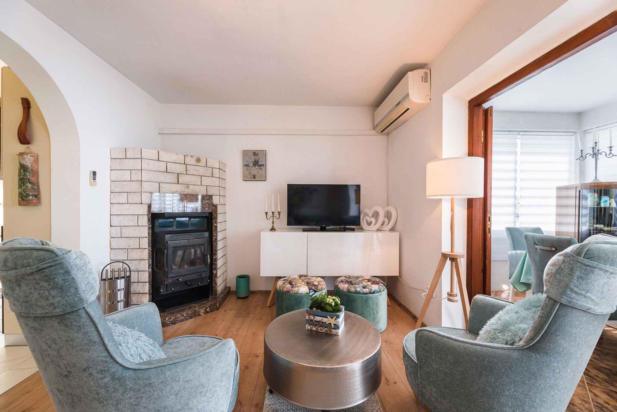 A living room with a fireplace, a TV, and two ottomans with cushions.