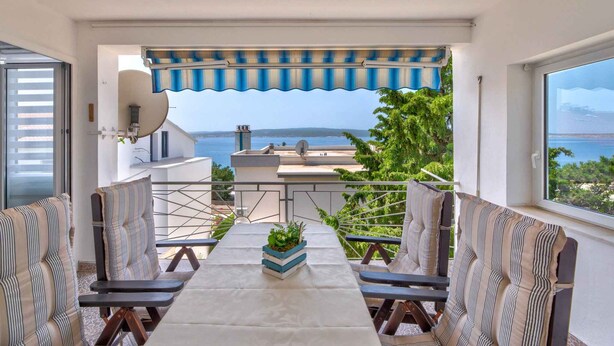 Un balcón con vista al mar, una mesa con sillas y una antena parabólica.