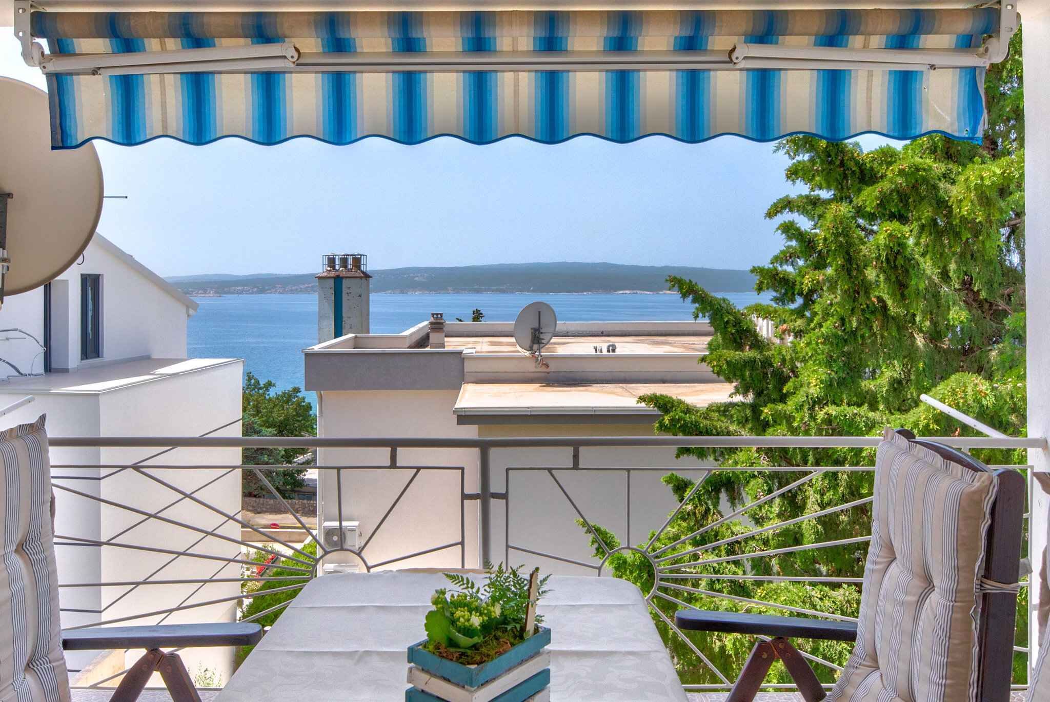 Un balcon avec vue sur la mer, une antenne parabolique et un auvent rayé.