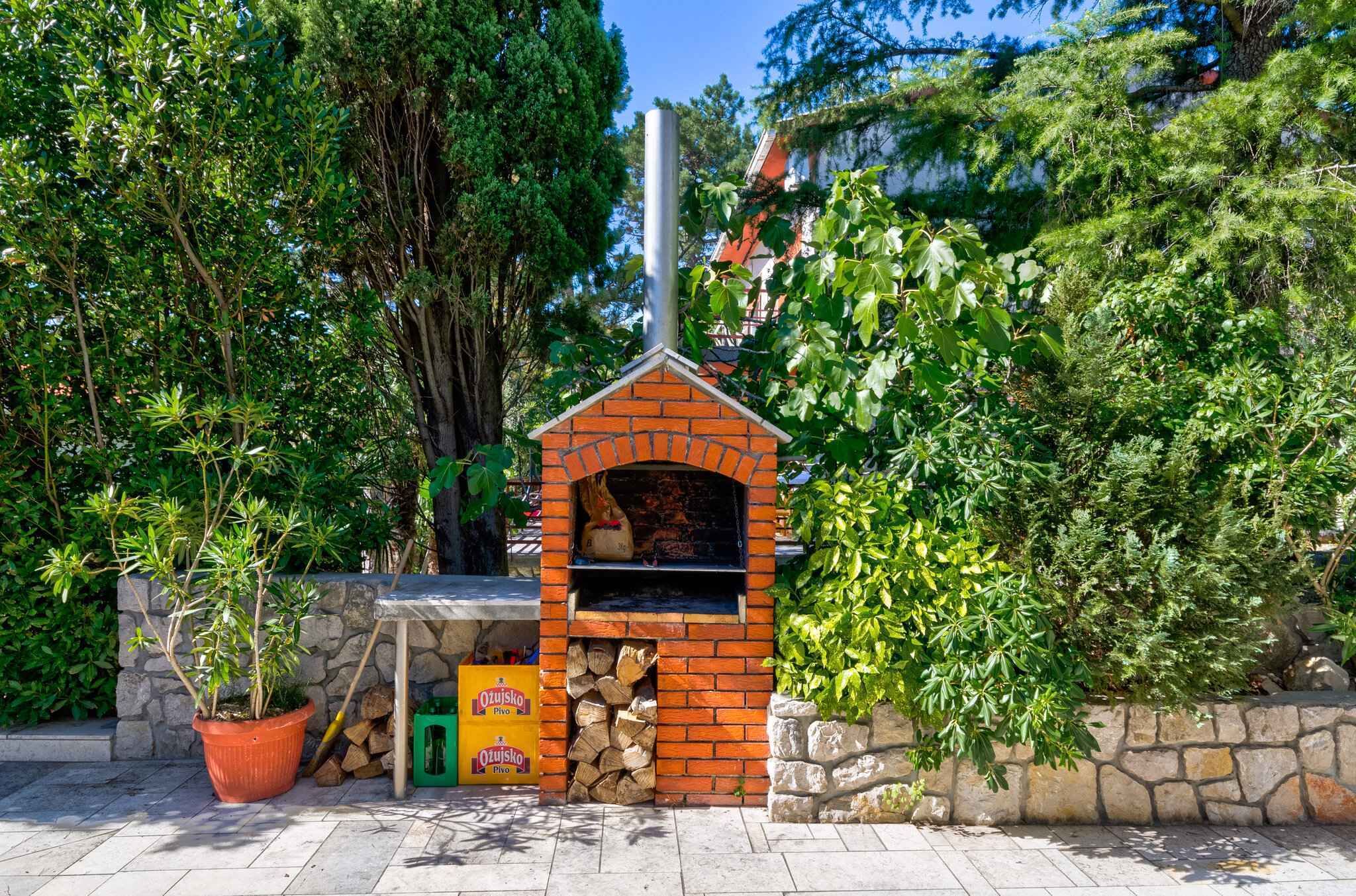 A brick-built outdoor oven with a chimney, surrounded by greenery and a stone wall.