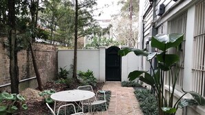 A courtyard with a brick pathway, white metal chairs, and a round table. - Cozy Furnished Apartment (New Orleans)