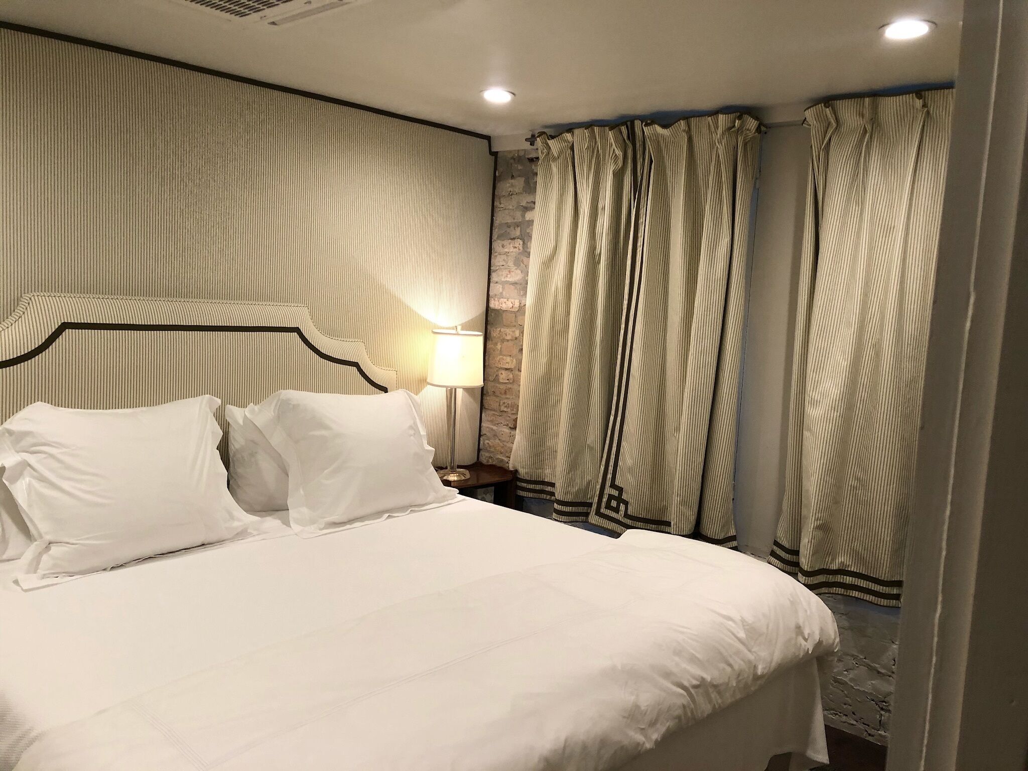 A neatly made bed with white linens, a headboard with a dark frame, and a bedside lamp.