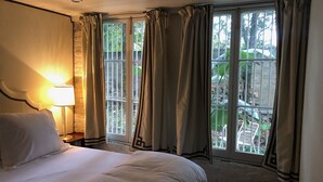 A hotel room with a large bed, a nightstand with a lamp, and a window with curtains. - Cozy Furnished Apartment (New Orleans)
