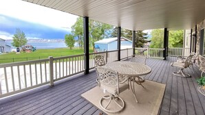 A covered outdoor patio with a table and chairs, overlooking a grassy area and a body of water.