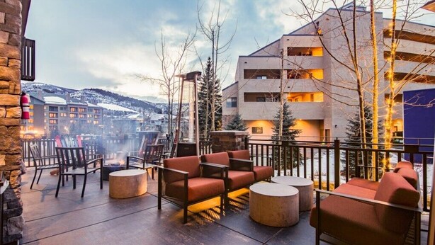 An outdoor seating area with sofas and chairs, a fire pit, and a view of a mountain range.