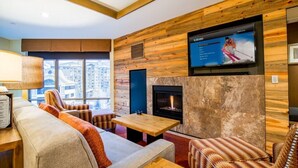 A modern living room with a fireplace, wooden panel walls, and a large TV screen.