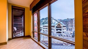 A room with large windows, a wooden floor, and a view of a building with a snow-covered mountain in the background.