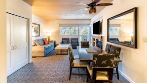 A modern hotel room with a large bed, a sofa, a dining table, and a TV. There are windows with a view of trees outside. - Marriotts Streamside at Vail - 1 Bedroom (Vail)