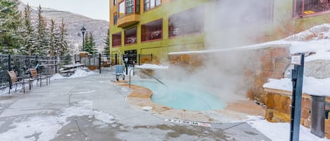 A spa area with a hot spring, outdoor seating, and a building with multiple windows.