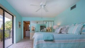 Een slaapkamer met een bed, een plafondventilator, een balkon en uitzicht op de omgeving.