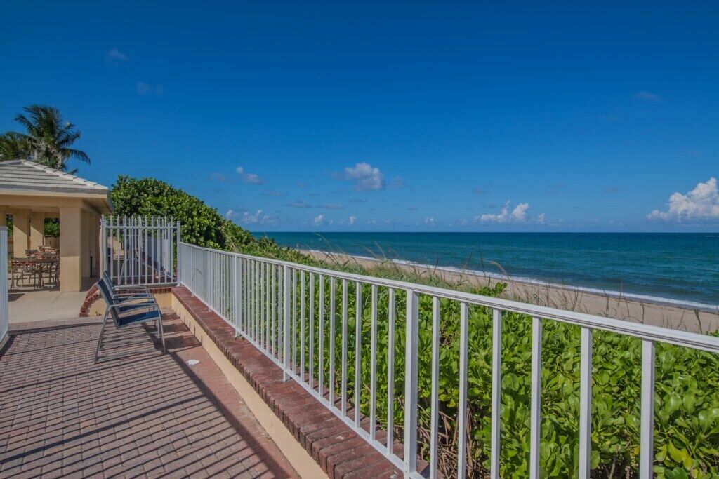 Een balkon met uitzicht op de oceaan, een wit hek en een gebouw met een deur en ramen.