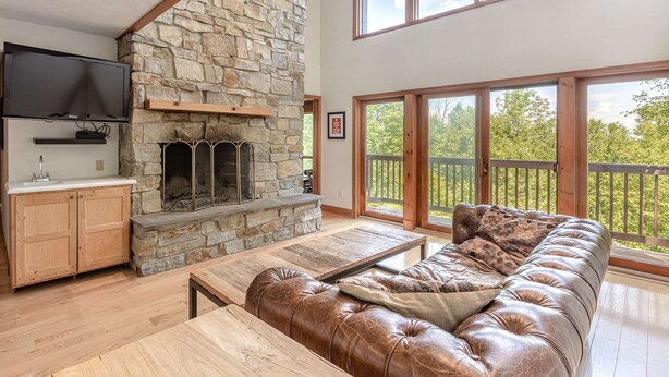 A spacious living room with a stone fireplace, a large leather sofa, and a wooden coffee table. - Only 5 minutes away from Stratton Mountain  (Winhall)