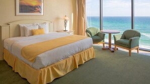 Une chambre d’hôtel avec un grand lit, deux chaises, une petite table et une vue sur l’océan.