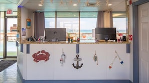 Un comptoir d’accueil avec vue sur la mer, une décoration en forme d’ancre portant l’inscription « Bienvenue » et un panneau « Il est interdit de fumer ».