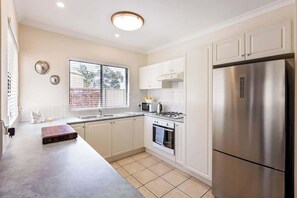Une cuisine moderne avec des meubles blancs, un réfrigérateur en acier inoxydable, un four à micro-ondes et une cuisinière à gaz.