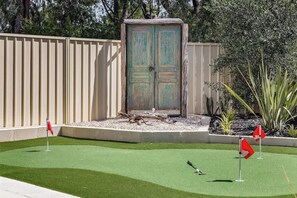 A miniature golf course with a green artificial turf, a wooden cabinet, and red flags marking the holes.