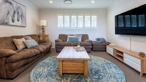 A living room with two sofas, a coffee table, a TV, and a window with blinds. - Summerville Treetops: A Stunning Valley Retreat (Yallingup Siding)