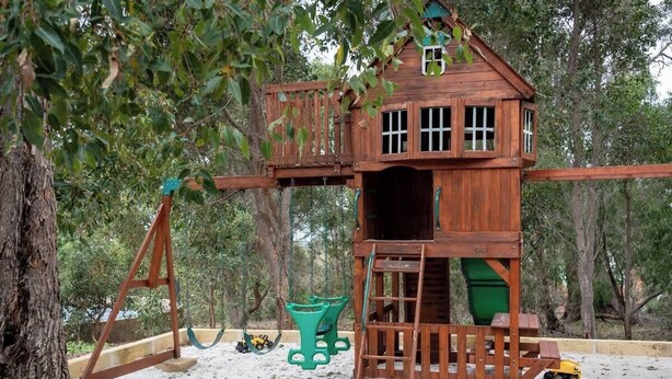 A wooden playhouse with a swing set, a slide, and a small staircase. - Summerville Treetops: A Stunning Valley Retreat (Yallingup Siding)