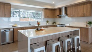 A modern kitchen with a large island, wooden cabinets, and a dishwasher. - Summerville Treetops: A Stunning Valley Retreat (Yallingup Siding)