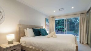 A bedroom with a large bed, a bedside table with a lamp, and a view of greenery through a sliding glass door. - Summerville Treetops: A Stunning Valley Retreat (Yallingup Siding)