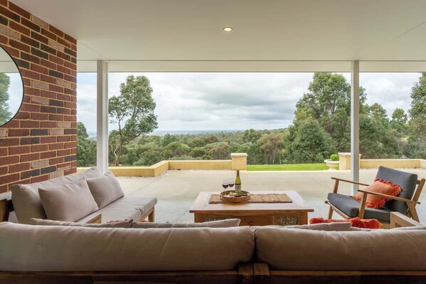 A modern outdoor living space with a brick wall, a sofa, a table with a lamp, and a chair.