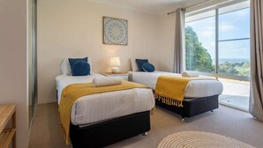 A hotel room with two beds, a large window with a view, a bedside table with a lamp, and a wall art piece. - Summerville Treetops: A Stunning Valley Retreat (Yallingup Siding)