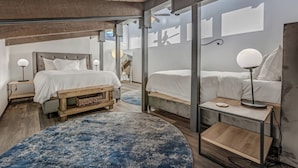 A bedroom with a large bed, a smaller bed, a wooden bench, a round blue rug, and a desk with a lamp. - Ski-In/Out Remodeled Mountain View Penthouse 1025 (Steamboat Springs)