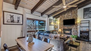 A cozy interior with a stone fireplace, a dining area with a wooden table and chairs, and a comfortable seating area with a sofa and pillows. - Ski-In/Out Remodeled Mountain View Penthouse 1025 (Steamboat Springs)