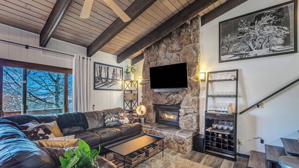 A cozy living room with a stone fireplace, a comfortable sofa, a flat-screen TV, and a wine rack. - Ski-In/Out Remodeled Mountain View Penthouse 1025 (Steamboat Springs)