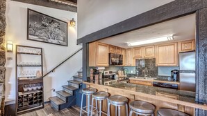 A modern kitchen with wooden cabinets, a stainless steel refrigerator, and a bar area with stools. - Ski-In/Out Remodeled Mountain View Penthouse 1025 (Steamboat Springs)