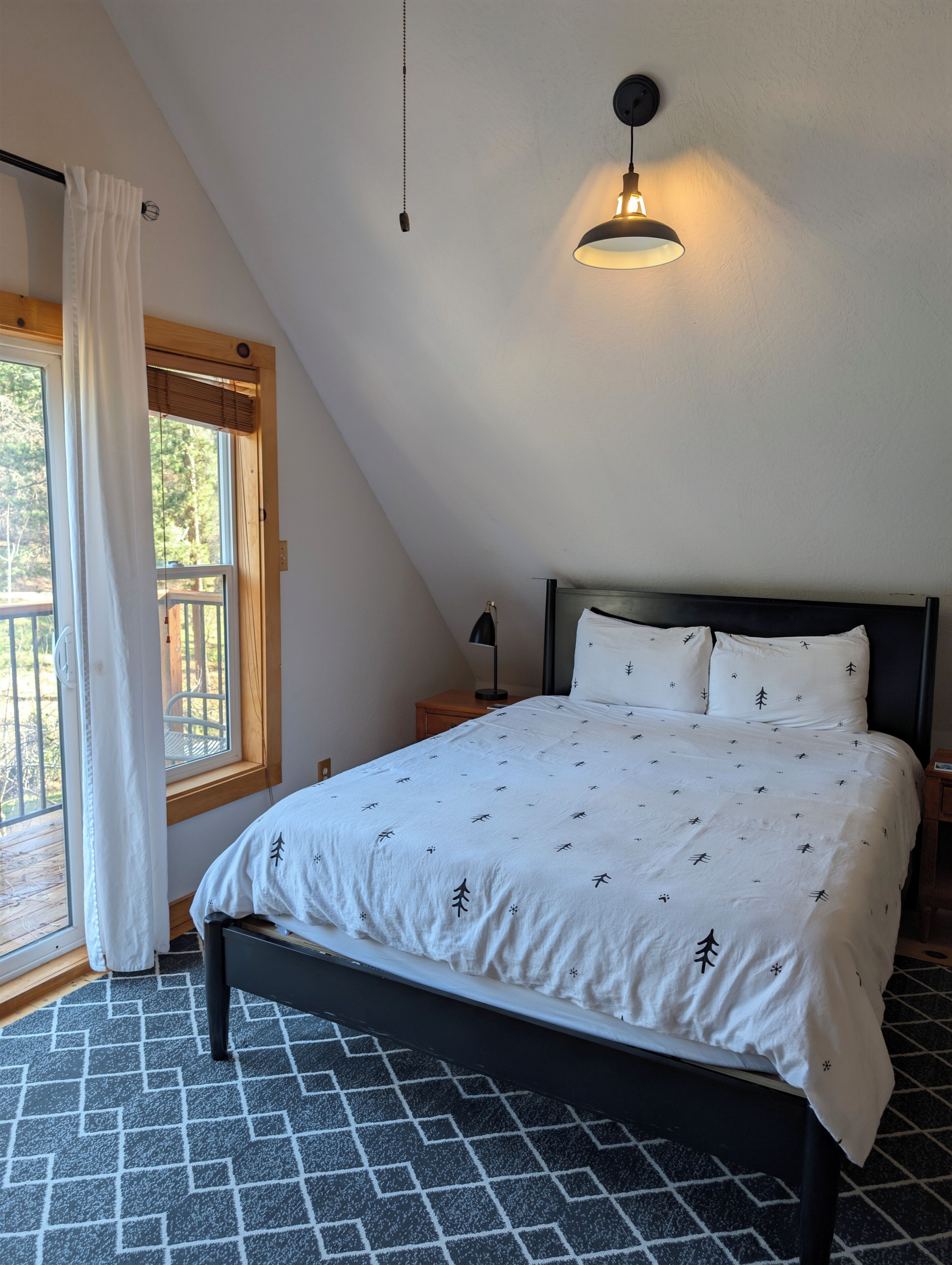A bedroom with a bed, a window with curtains, a hanging light fixture, and a patterned floor.