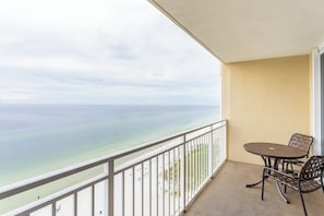 A balcony with a view of the ocean, a table, and two chairs.